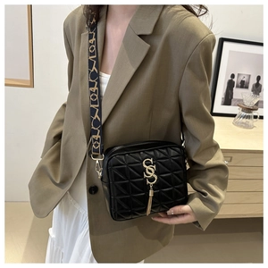 Détail du sac bandoulière noir matelassé avec logo doré, pompon et sangle jacquard