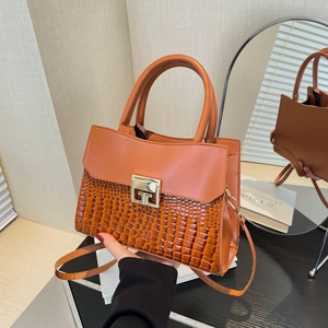 Brown leather crossbody bag with crocodile texture and golden clasp on a reflective surface