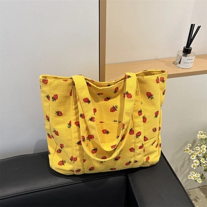 Yellow corduroy tote bag with red strawberry print on a sofa in a modern room