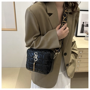 Détail du sac bandoulière noir matelassé avec logo SS doré et pompon sur sangle fleurie