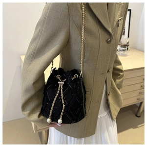 Detail einer schwarzen Eimertasche mit Fransen, Goldkette und Perlenakzenten am Modell