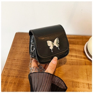 Détail du papillon argenté sur un mini sac à bandoulière noir brillant avec chaîne argentée