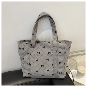 Detail of grey corduroy tote bag with black bow patterns and diamond quilting on a sofa