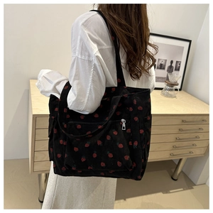 Detail of black corduroy tote bag with red strawberry pattern worn on shoulder
