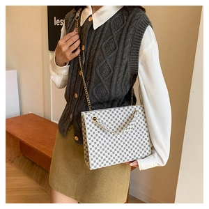 Detailed view of the cream tote bag with geometric print and gold chain strap worn by a model