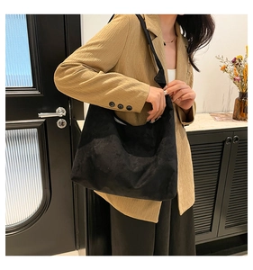 Détail d'un grand sac cabas noir en daim avec bandoulière large porté par un mannequin