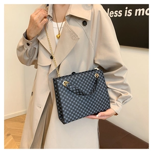 Detail of dark blue patterned tote bag with gold chain strap worn by a model
