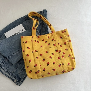 Yellow corduroy tote bag with strawberry prints and a front pocket on white background