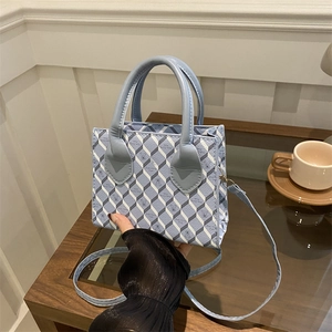 Sac à main géométrique à carreaux avec poignées bleues sur un bureau élégant