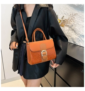 Détail d'un sac à main marron texture crocodile avec boucle dorée porté par un mannequin