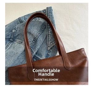 Detail of brown leather tote bag handles featuring irregular patchwork and contrast stitching