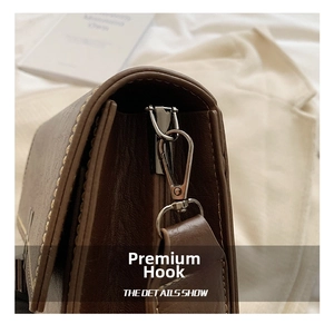 Detail view of coffee brown leather bag showing silver metal hook and yellow contrast stitching