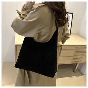 Side view of large black suede tote bag styled with a beige trench coat for a chic look