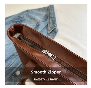 Close-up of smooth silver zipper and leather stitching on brown caramel tote bag