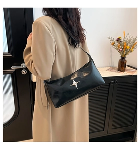 Detailed view of black leather shoulder bag with silver star accent on a trench coat