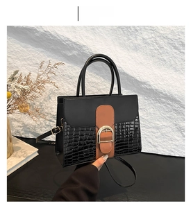 Detail of black and brown crossbody bag with crocodile pattern and gold buckle