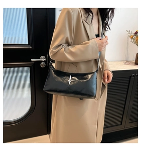 Close-up of black glossy shoulder bag with silver star detail on a khaki trench coat