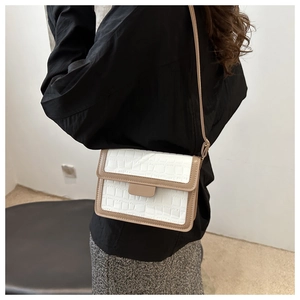 Detail einer weißen Umhängetasche mit Krokodilprägung und khakifarbenem Rand am Model