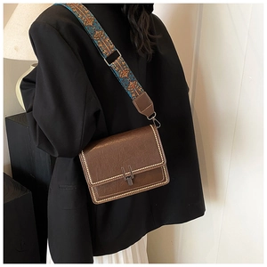 Dettaglio borsa in pelle marrone con borchie metalliche e tracolla intrecciata colorata