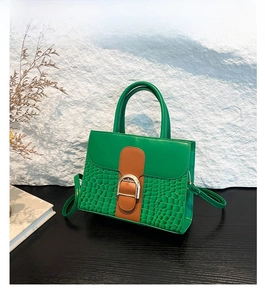 Close-up of green crocodile texture leather handbag with gold buckle and brown details