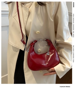 Detail of red crescent bag with glossy leather finish and lucky clover charm