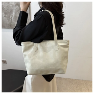 Detail of a cream faux leather tote bag showing geometric panel stitching and long straps