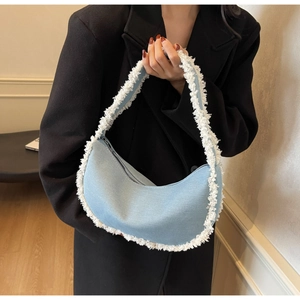 Detail showing frayed fringe edges and denim texture on the blue crescent shoulder bag