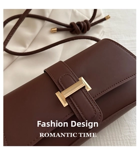 Close-up of brown leather bag with golden H-shaped buckle on white textured background