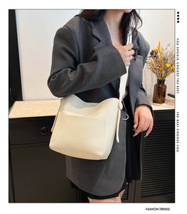 Detail of cream-colored pebble leather bucket bag with side buckle and wide shoulder strap