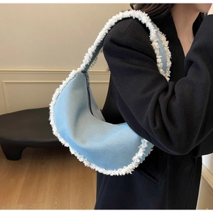 Detail of light blue denim half-moon bag with white plush fringe on model shoulder