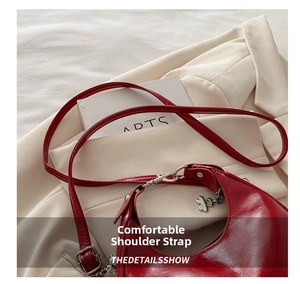 Detail of red crescent bag with adjustable strap, silver buckle and clover charm