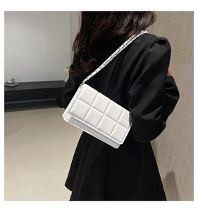 Modern white quilted shoulder bag with chunky chain strap worn by a model in black dress