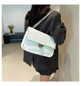 Detail of white pleated shoulder bag featuring glossy texture and silver metal clasp