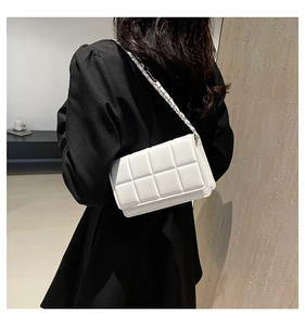 Detail of white quilted crossbody bag featuring square puff texture and metal chain strap