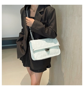 Close-up of minimalist light-colored shoulder bag with chain strap and metallic lock detail