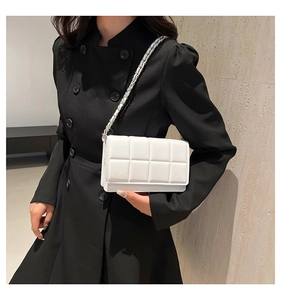 Close-up of white quilted chain bag with square texture on a black coat outfit