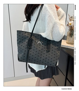 Close-up of a large grey tote bag with black bow prints worn by a model in soft light