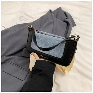 Dettaglio della borsa in pelle nera e denim blu con tracolla larga color crema