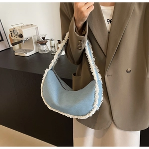 Close-up of light blue denim crescent underarm bag with white cotton fringe trim