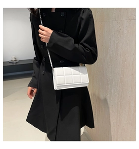 Close-up of a white quilted square bag with silver chain strap worn on a black coat