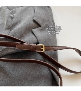 Detail of a brown leather shoulder strap with golden metal buckle on a grey suit