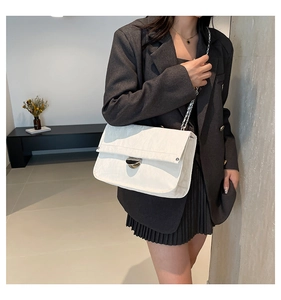 Detail of white chain shoulder bag with silver twist lock on gray blazer