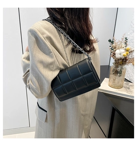 Detail of black quilted shoulder bag with silver chain strap worn over beige blazer