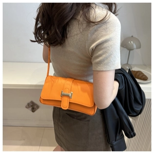 Detail of a bright orange leather underarm bag with a golden metal clasp worn by a model