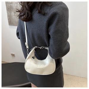 Detail of white leather crescent bag with metal chain strap and clover charm pendant