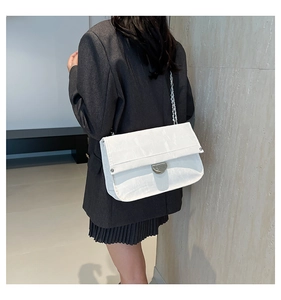 Close-up of white flap shoulder bag with silver chain strap and metal swivel lock detail