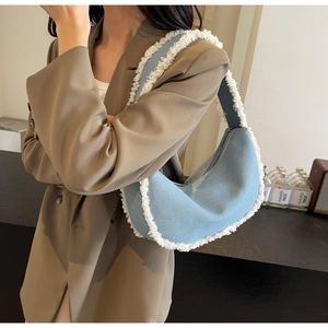 Detail of denim crescent bag featuring white faux fur fringe and metal zipper closure