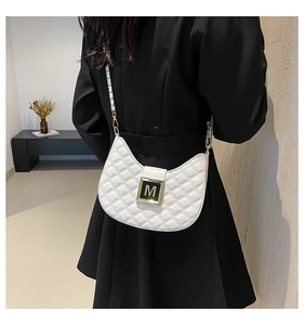 Close-up of a white quilted crescent bag featuring a golden M-letter buckle and chain strap