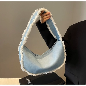 Detailed close-up of light blue denim crescent bag with white frayed fringe edges