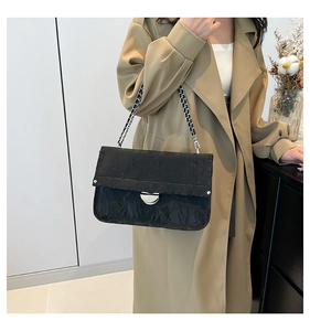 Detail of black pleated shoulder bag with silver clasp and woven chain on trench coat